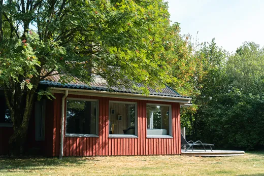 Sommerhuset set fra siden med terrasse og liggestole.